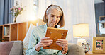 Sad, senior woman and picture frame for memory, nostalgia and remember history in home living room. Retirement, photo and past of missing person with grief, lonely and mourning family member on sofa