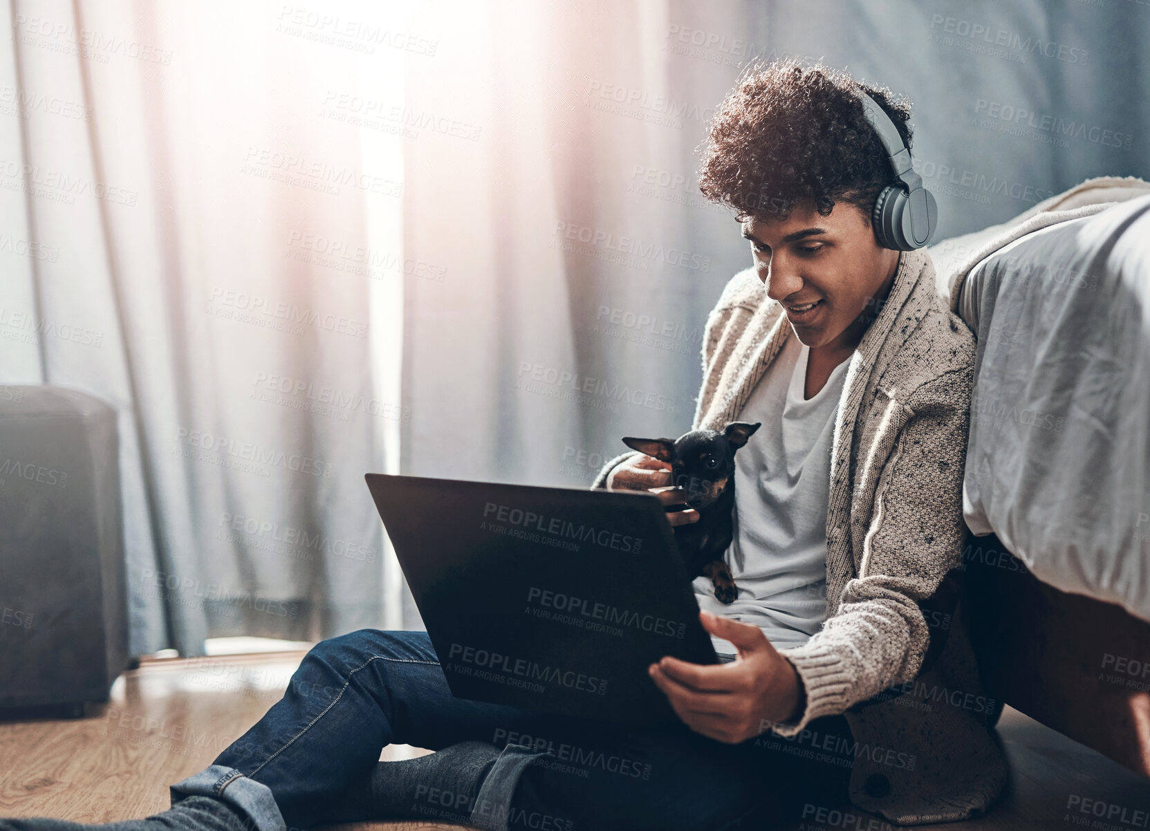 Buy stock photo Shot of a young man using a laptop and headphones with his dog while working at home