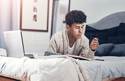 Buy stock photo Shot of a young man writing in a notebook and using a laptop on his bed at home