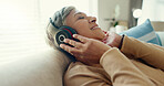 Retirement, senior woman and couch with headphones, relax and calm in living room, streaming music and audio. Rest, happy and mature lady with headset for podcast, radio and carefree on sofa