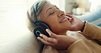 Retirement, mature woman and sofa with headphones, relax and calm in living room, streaming music and audio. Rest, happy and senior lady with headset for podcast, radio and carefree on couch