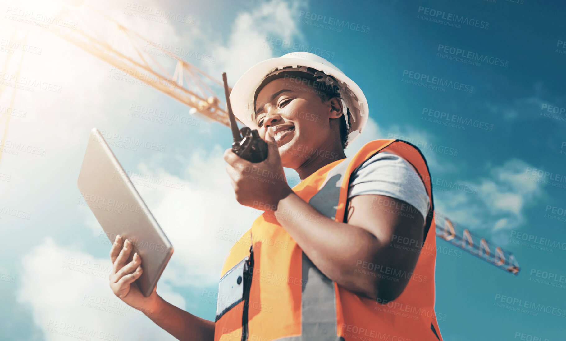 Buy stock photo Shot of a young woman using a digital tablet and walkie talkie while working at a construction site