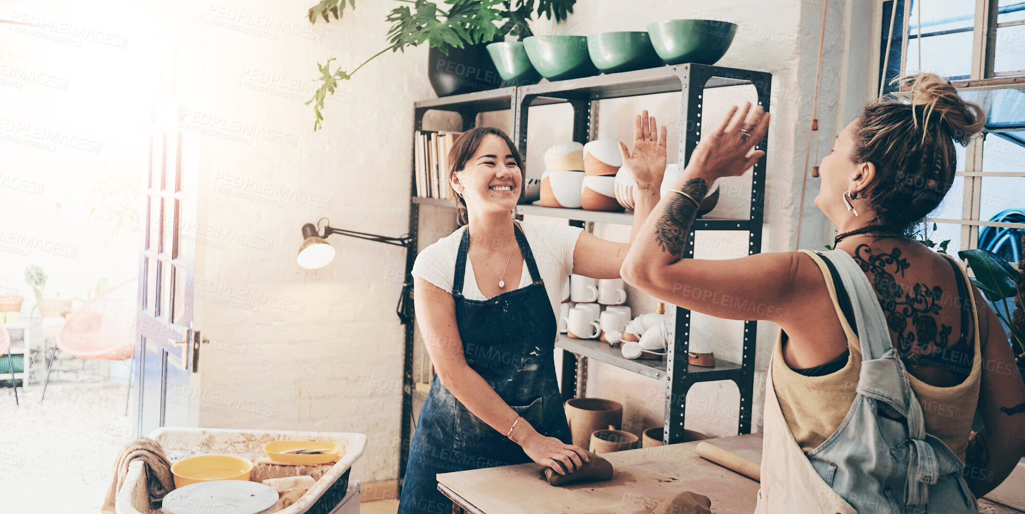 Buy stock photo Shot of two young women giving each other a high five in a pottery studio