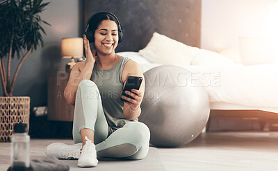 Buy stock photo Shot of a sporty young woman wearing headphones and using a cellphone while exercising at home