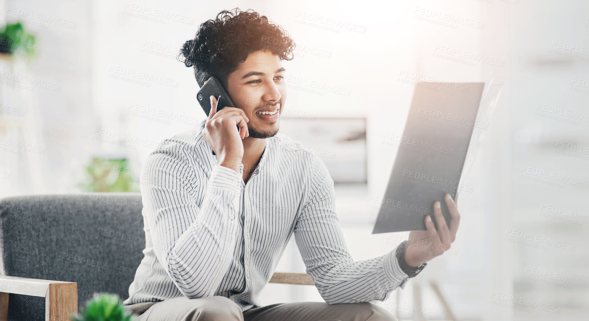 Buy stock photo Shot of a young businessman talking on a cellphone while going through paperwork in an office