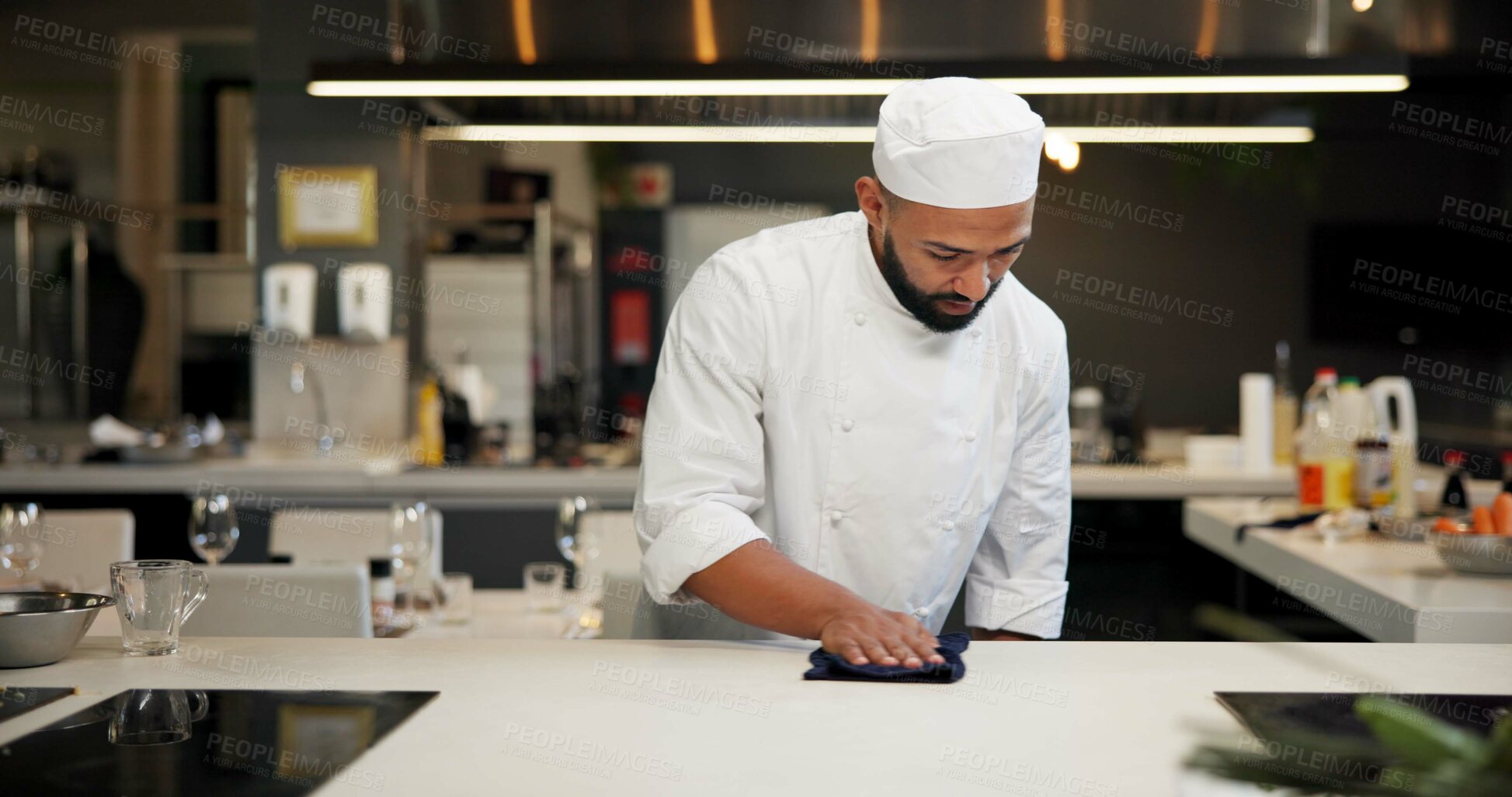 Buy stock photo Man, chef and serious with wipe kitchen counter at restaurant for fine dining, health and hygiene. Male employee, professional and cooker with cloth for culinary, hospitality and catering service