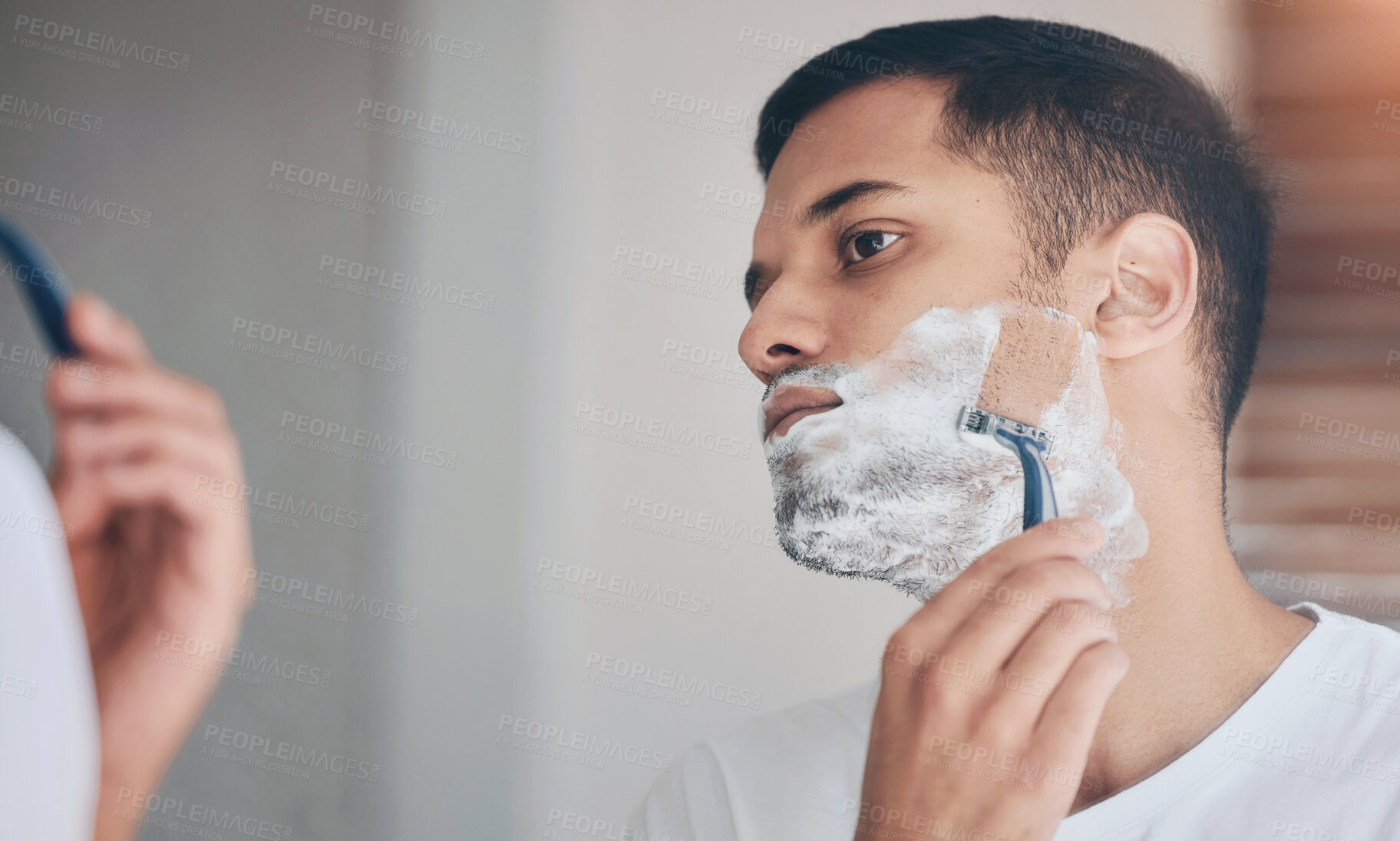 Buy stock photo Shot of a young man shaving his beard in a bathroom at home