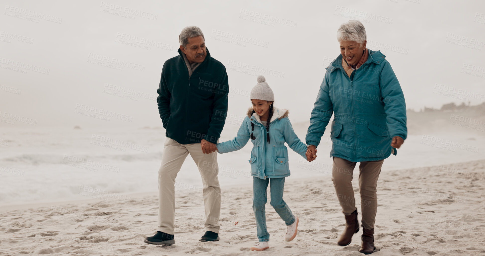 Buy stock photo Grandparents, child and beach with holding hands, walking and together on vacation by the sea. Love, smile and happy girl with senior people outdoor in winter on holiday with retirement and travel