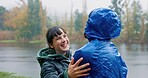 Smile, couple and hug in rain outdoor for hiking with love, freedom and adventure with bonding for care. Man, woman and together for embrace by lake in winter, carefree and romance with affection.