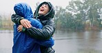 Happy, couple and hug in rain outdoor for hiking with love, freedom and adventure with bonding for care. Man, woman and together for embrace by lake in winter, carefree and romance with affection.