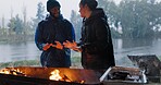 Couple, hands and fire in outdoor with rain for warm on camp, adventure and winter getaway for holiday. Man, woman and together with bonfire for fireside connection, happiness and lakeside with flame