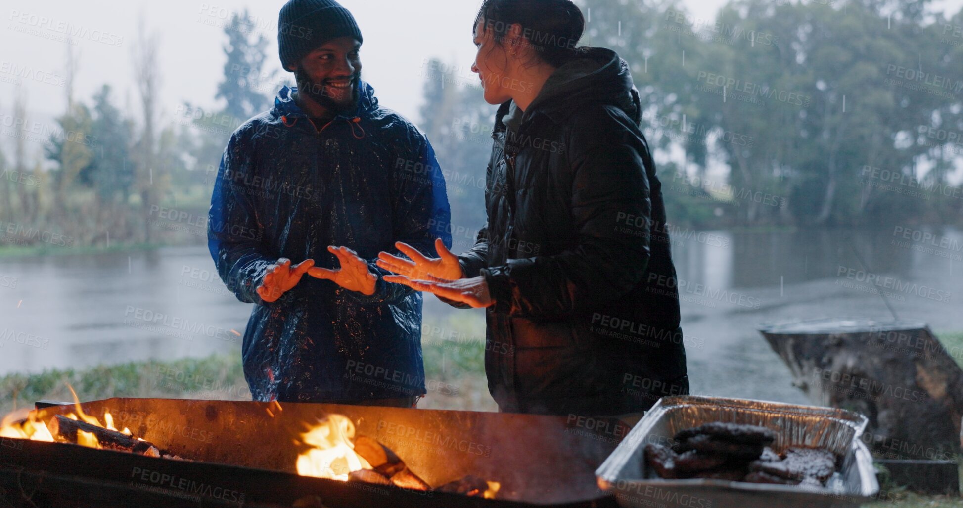 Buy stock photo Couple, hands and fire in outdoor with rain for warm on camp, adventure and winter getaway for holiday. Man, woman and together with bonfire for fireside connection, happiness and lakeside with flame