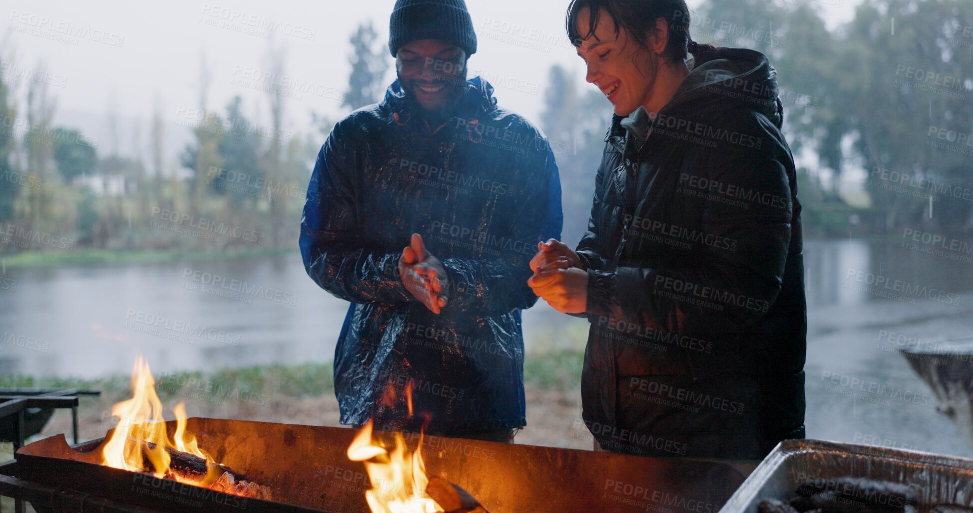 Buy stock photo Couple, hands and bonfire in outdoor with rain for warm on camp, adventure and winter getaway for holiday. Man, woman and together with fire for fireside connection, happiness and lakeside with flame