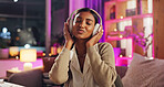 Headphones, Indian woman and night with dance, music and home with audio subscription. Neon, streaming and smile with happy, relax and chill track in a living room and listening to pop song on sofa