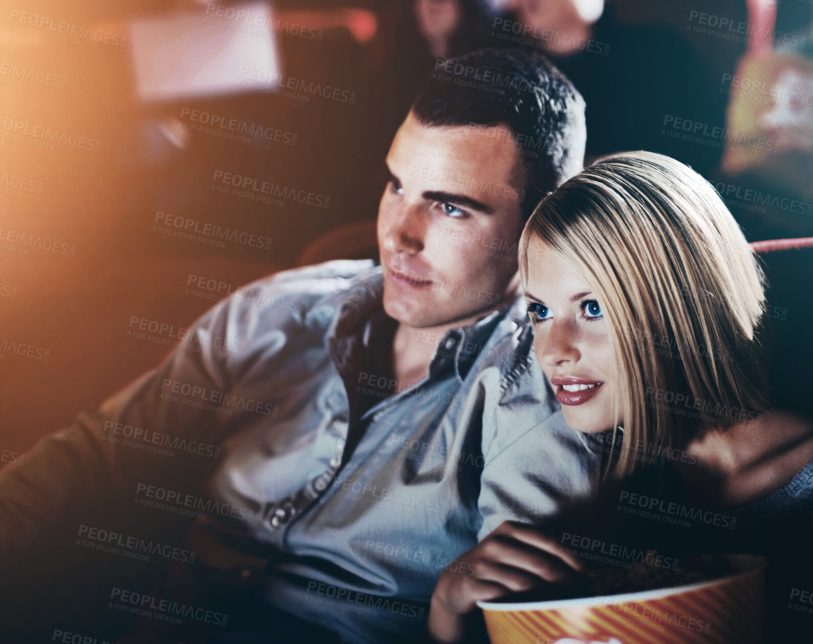 Buy stock photo Date, popcorn and couple at cinema for watching movie, eating or romantic night together. Lens flare, evening and young woman with man in theater with snack for entertainment, show or film premier