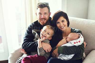 Buy stock photo Shot of a cheerful young family seated on a sofa together at home during the day