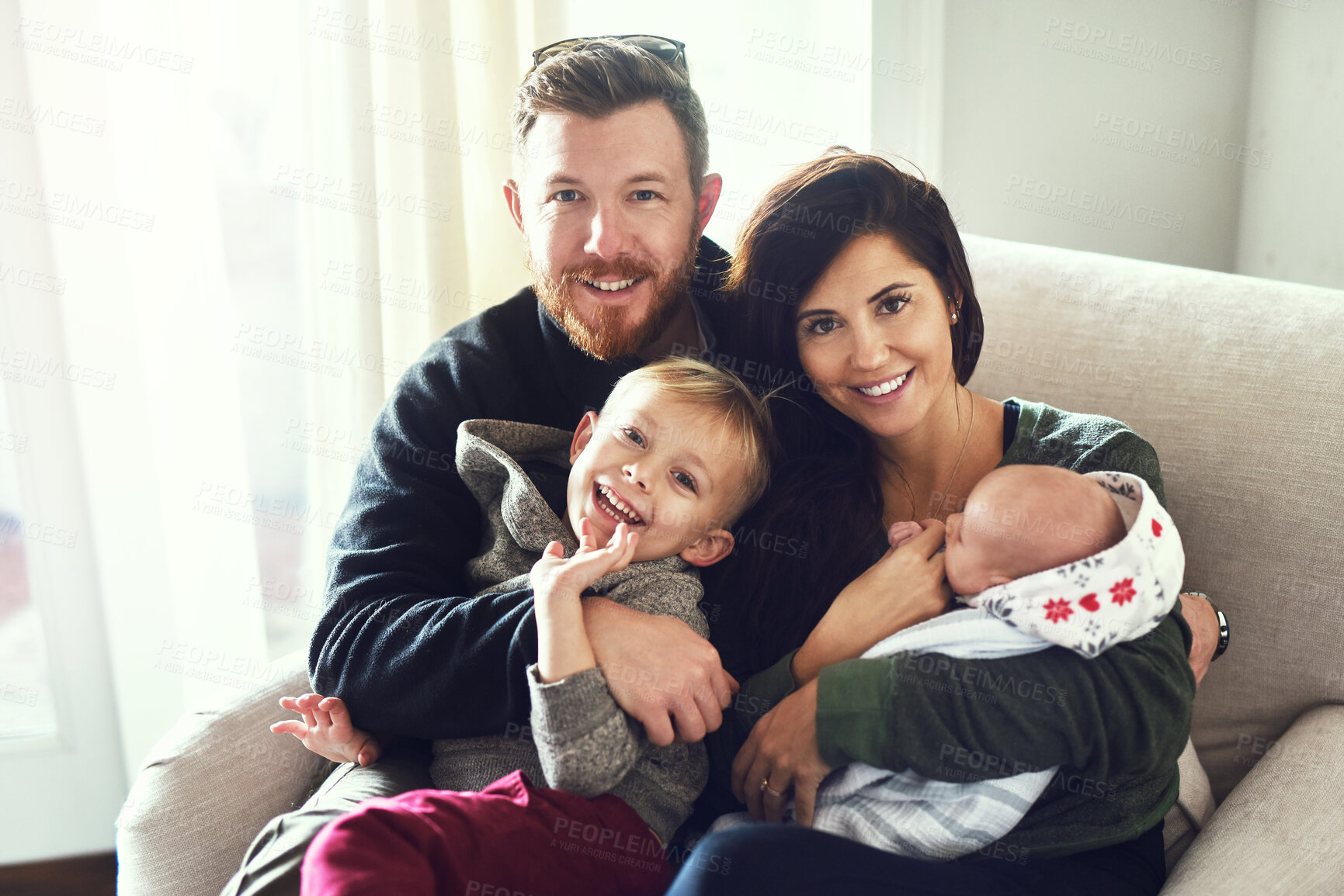 Buy stock photo Shot of a cheerful young family seated on a sofa together at home during the day