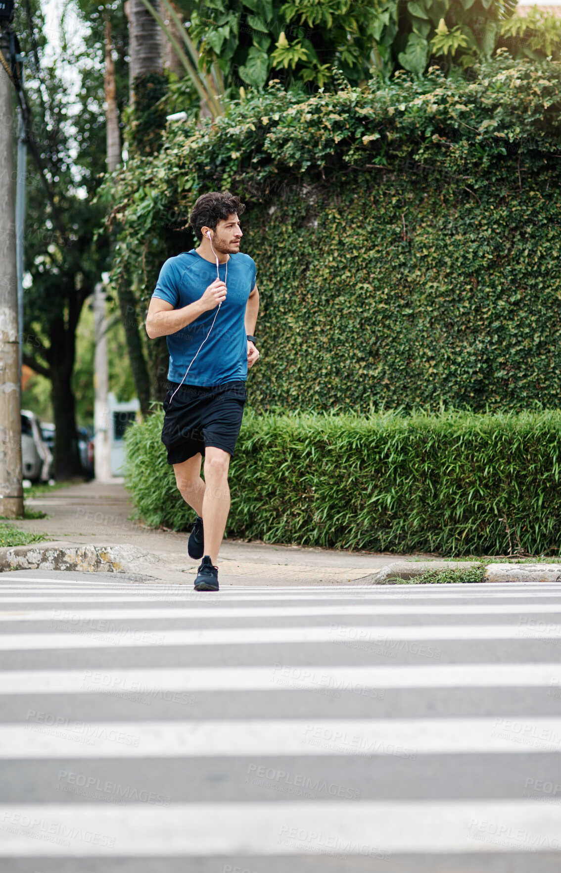 Buy stock photo Shot of a sporty young man running across a road as exercise outside during the day