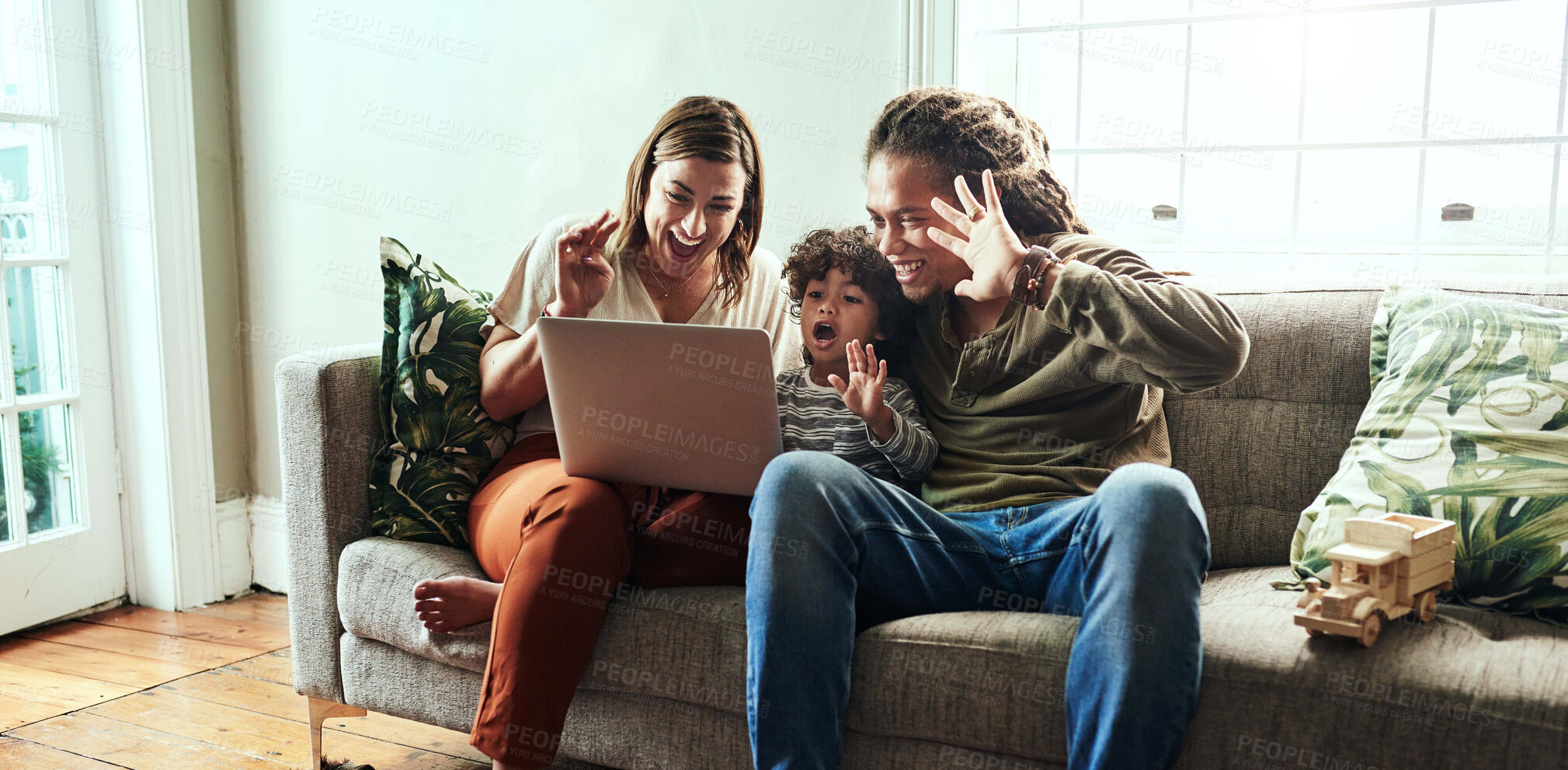 Buy stock photo Shot of a cheerful young couple and their son having a video call to relatives on a laptop while being seated on a sofa at home