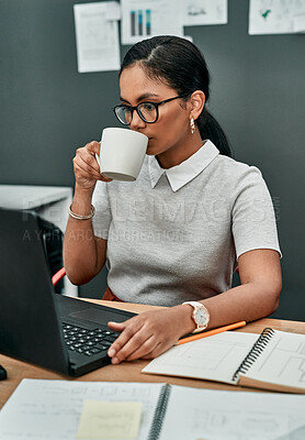 Buy stock photo Shot of a young businesswoman drinking coffee while working on a laptop in an office