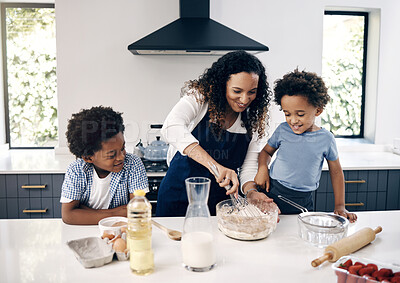 Buy stock photo Adorable little boy with afro baking in the kitchen at home with his mom and brother. Cheerful mixed race woman mixing ingredients with the help of her little boys. Baking is a bonding activity