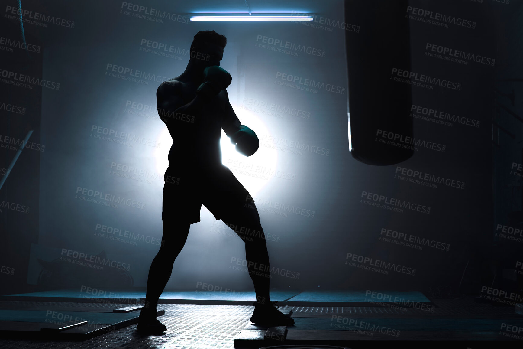 Buy stock photo Man, punching bag and silhouette of athlete at gym, training practice and attack challenge for combat. Male person, light and dojo club aesthetic for fight competition, skill and martial arts workout