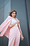 Portrait of a young trendy and confident mixed race woman looking stylish while posing and chilling time in the city. Fashionable hispanic woman wearing pink clothes and standing outside downtown