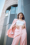 Portrait of a young trendy and confident mixed race woman looking stylish while posing and chilling time in the city. Fashionable hispanic woman wearing pink clothes and standing outside downtown 