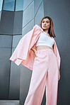 Portrait of a young trendy and confident mixed race woman looking stylish while posing and chilling time in the city. Fashionable hispanic woman wearing pink clothes and standing outside downtown 