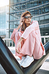 A young trendy and confident mixed race woman looking stylish while posing and spending time in the city. Fashionable hispanic woman wearing pink clothes and sunglasses sitting with cool sneakers