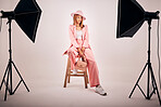 Portrait of a young mixed race female posing in trendy fashionable clothing, chilling on a chair in a grey studio background. Hispanic woman in the latest fashion collection with a cool style and hat