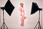 Serious young mixed race woman posing in trendy fashionable clothing while standing in a studio shoot. Confident hispanic woman posing in pink clothes in a studio with bright lights