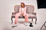 Young mixed race female posing in trendy clothing while sitting on a couch and making a call with a landline phone against a grey studio background. Confident hispanic woman posing in pink clothes