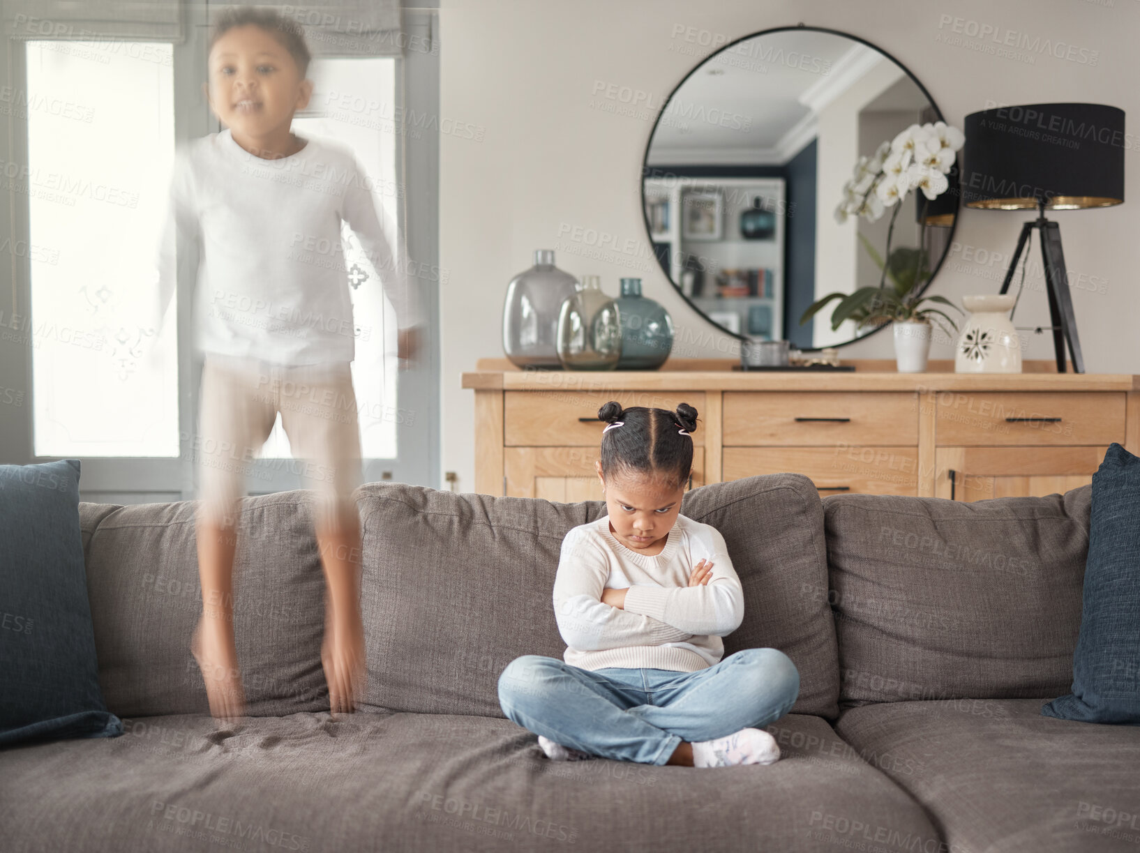 Buy stock photo Frustrated little girl, sofa and jumping with sibling in chaos, hyperactive or dispute in living room at home. Female person, children or kids in unfair playtime, energetic or mixed emotions at house