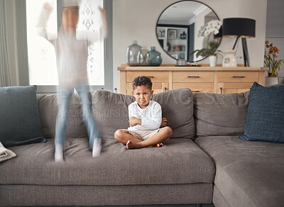 Buy stock photo Jumping, sofa and angry kid with ADHD, excited and hyper with frustrated boy from fight. Youth, family home and chaos with sad brother with frown from exclusion from sister game and fun in lounge