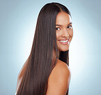 Portrait of a hispanic brunette woman with long lush beautiful hair smiling and posing against a grey studio background. Mixed race female standing showing her beautiful healthy hair