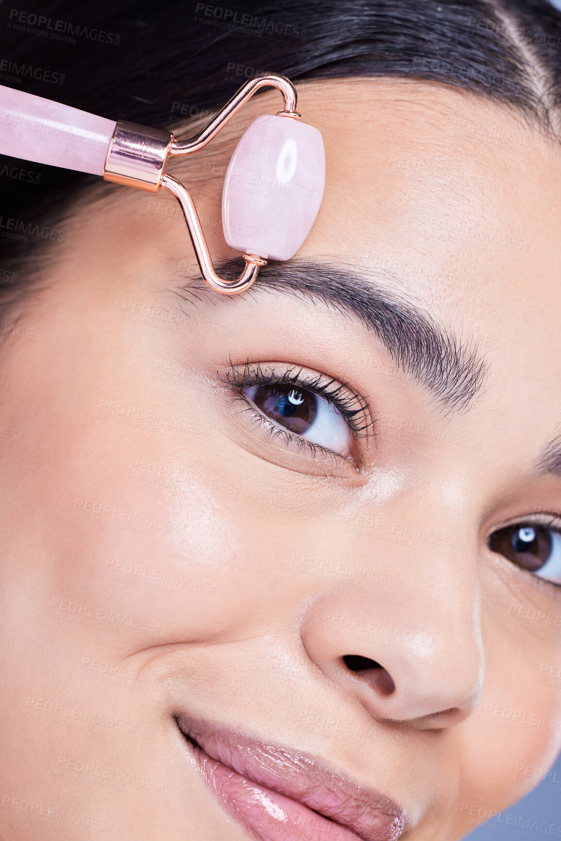 Buy stock photo Beauty, face roller and portrait of woman in studio with lymph drainage massage routine. Skincare, rose quartz and person with crystal tool for facial blood circulation with glow by blue background.