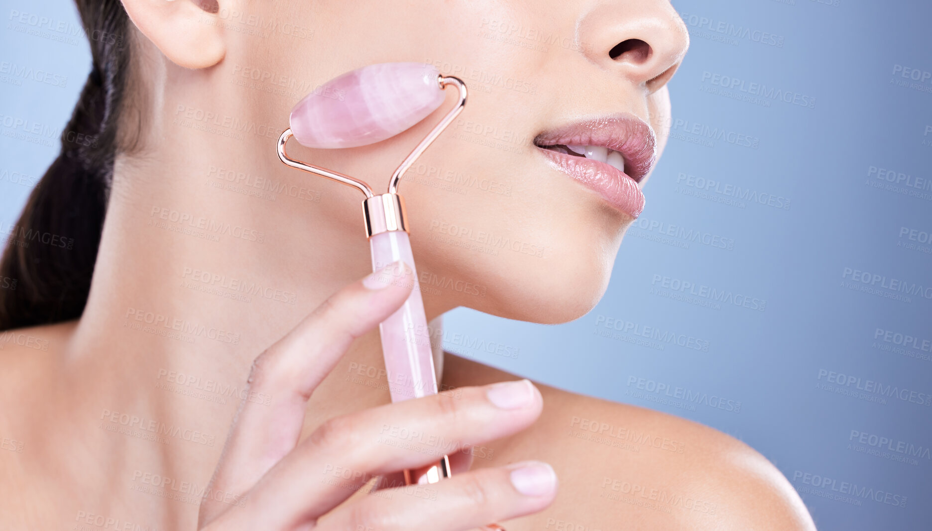 Buy stock photo Skincare, facial roller and face of woman in studio with lymph drainage massage routine. Beauty, rose quartz and female person with crystal tool for blood circulation with glow by blue background.