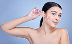 Studio Portrait of a beautiful mixed race woman using a rose quartz derma roller during a selfcare grooming routine. Young hispanic woman using anti ageing tool against blue copyspace background