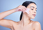 A beautiful mixed race woman using a rose quartz gua sha to reduce wrinkles and promote cell renewal. Young hispanic woman using anti ageing tool against blue copyspace background