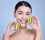 Studio Portrait of a happy smiling mixed race woman holding a kiwi fruit. Hispanic model promoting the skin benefits of a healthy diet against a blue copyspace background