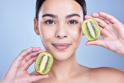 Buy stock photo Girl, portrait and kiwi in studio for skincare or natural cosmetics, facial treatment and enzyme exfoliation. Woman, happy and fruit on blue background for antioxidants, skin tone and hydration.