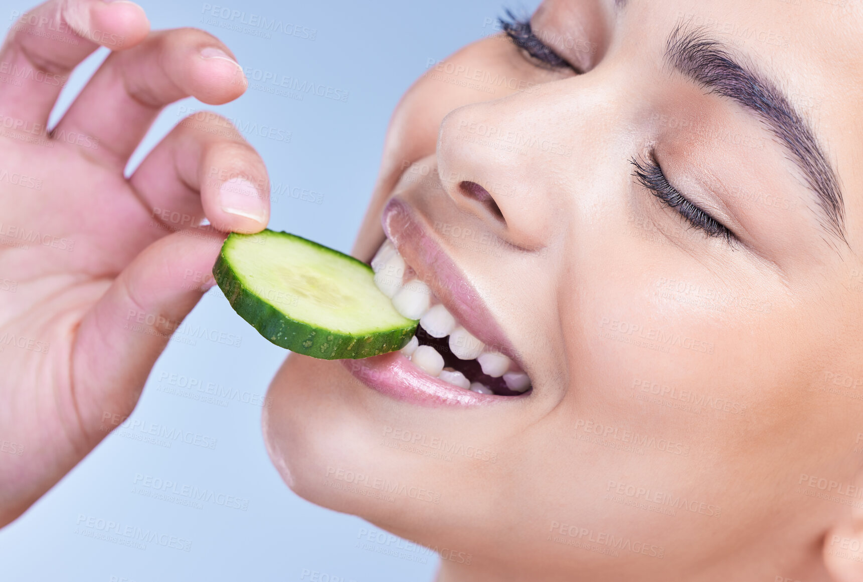 Buy stock photo Face, woman and mouth with eating cucumber in studio for skincare, anti aging benefits or detox for glowing skin. Model, girl and vegetable for nutrition, hydration and wellness on blue background