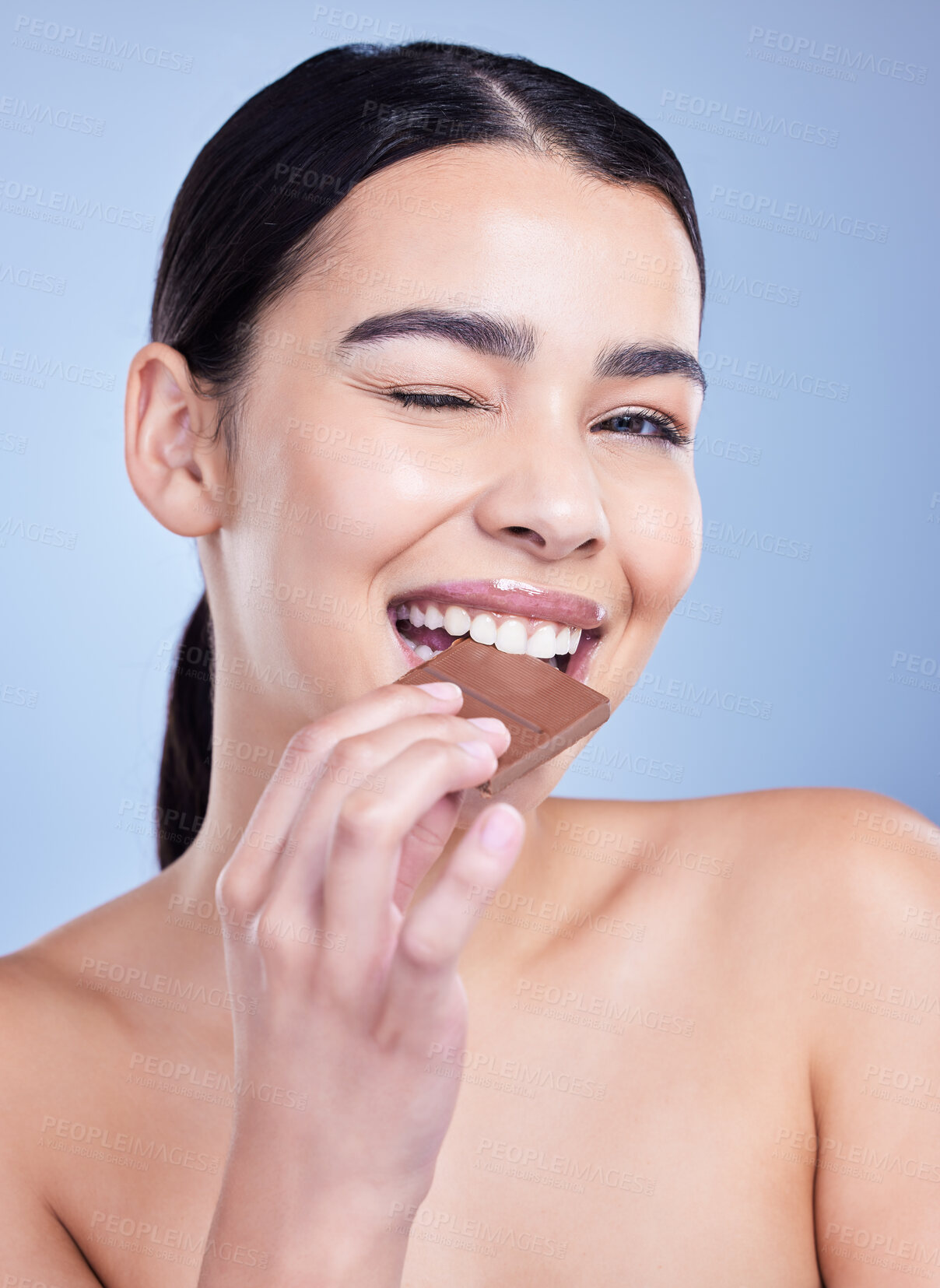 Buy stock photo Skincare, portrait and woman eating chocolate for beauty in studio isolated on blue background. Face, cosmetics and happy model with cocoa candy for diet, cheat meal or wink for food with antioxidant