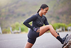 Active and fit young mixed race woman stretching her leg during outdoor exercise. Smiling, toned hispanic athlete getting ready to run in the morning. Routine sports and physical activity are healthy