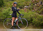 One athletic young woman using a cellphone while cycling outside on a bicycle. Sporty fit female wearing a helmet and taking a break to text, browse online social media and use a navigation app