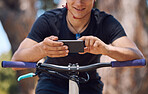 Young male cyclist using a cellphone while taking a break from cycling on a bicycle. Man stopping to text and scroll social media while exercising in a park. Checking his messages before his workout