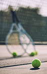 Group of tennis balls and rackets against a net on an empty court in a sports club during the day. Playing tennis is exercise, promotes health, wellness and fitness. Gear and equipment after a game