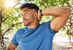 Fit athletic man smiling while stretching his arms during a workout at the park. Hispanic man doing warm-up exercises outdoors on a sunny day. Athletic man taking a break from a fitness routine