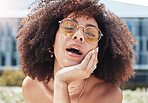 Portrait of young trendy beautiful mixed race woman with an afro smiling and posing alone outside. Hispanic woman wearing sunglasses and feeling happy. Fashionable African American woman in the city